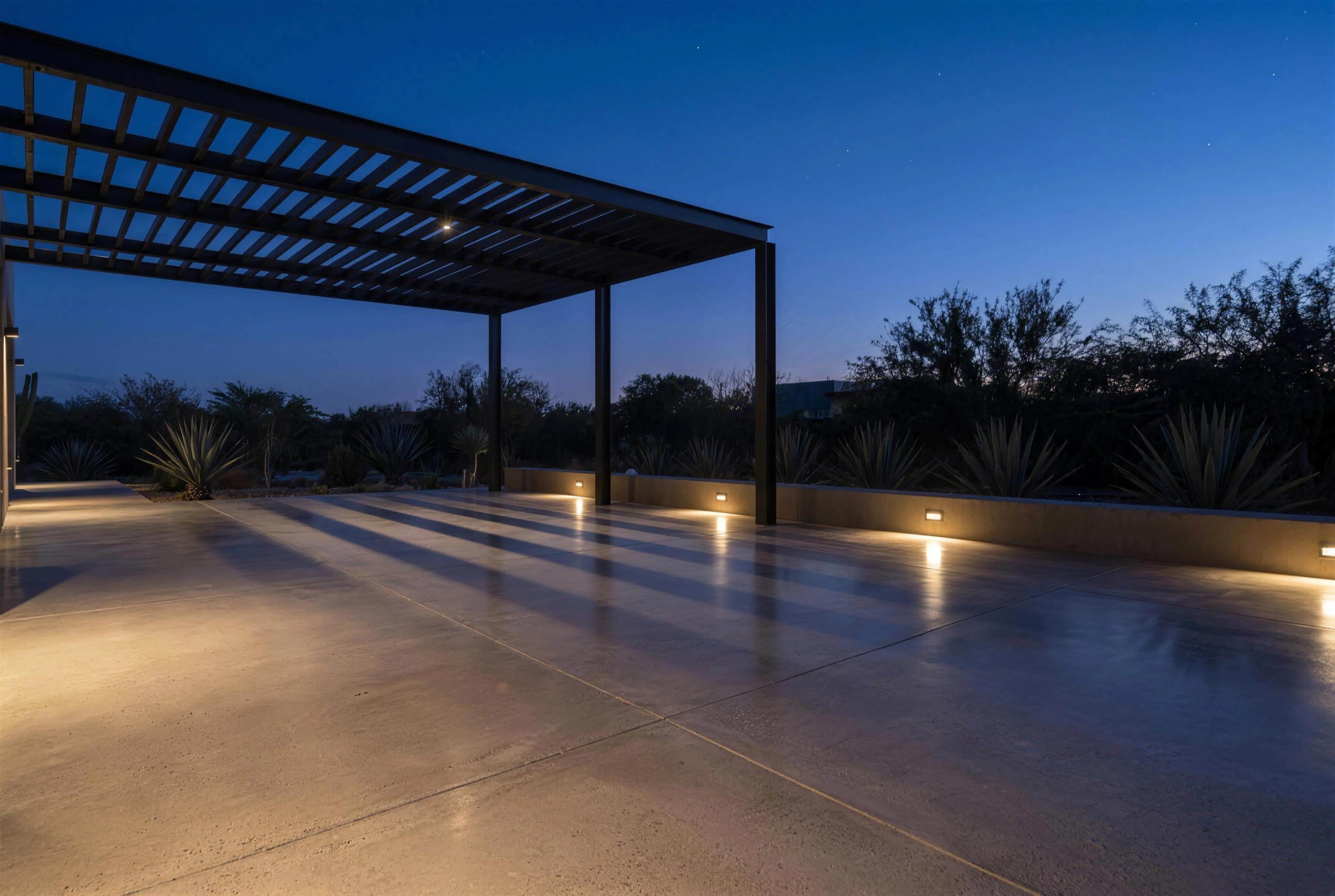 Patio de concreto pulido con pérgola de acero al anochecer