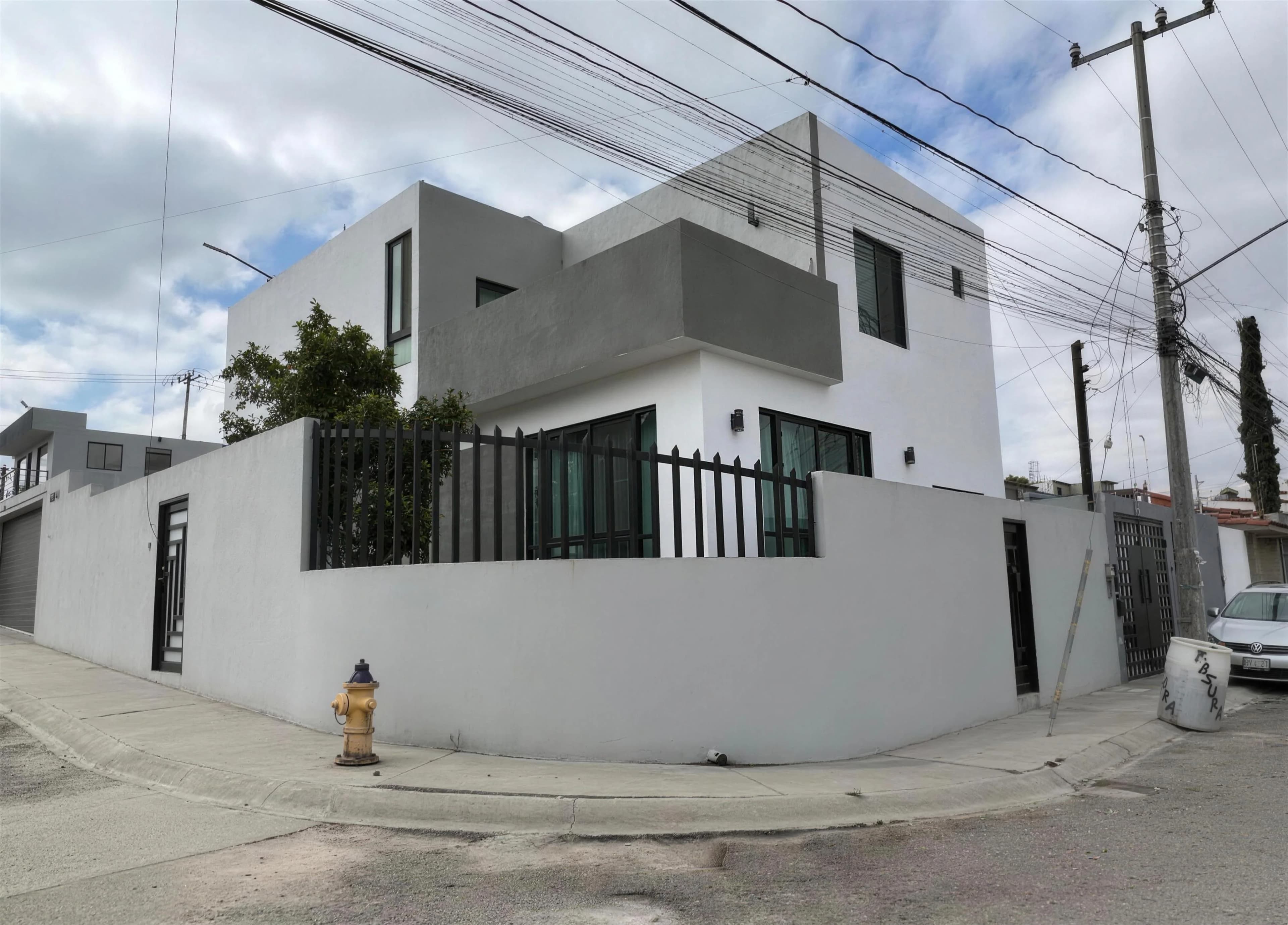 Casa La Presa terminada: vivienda en esquina de volúmenes blancos con terraza de concreto aparente
